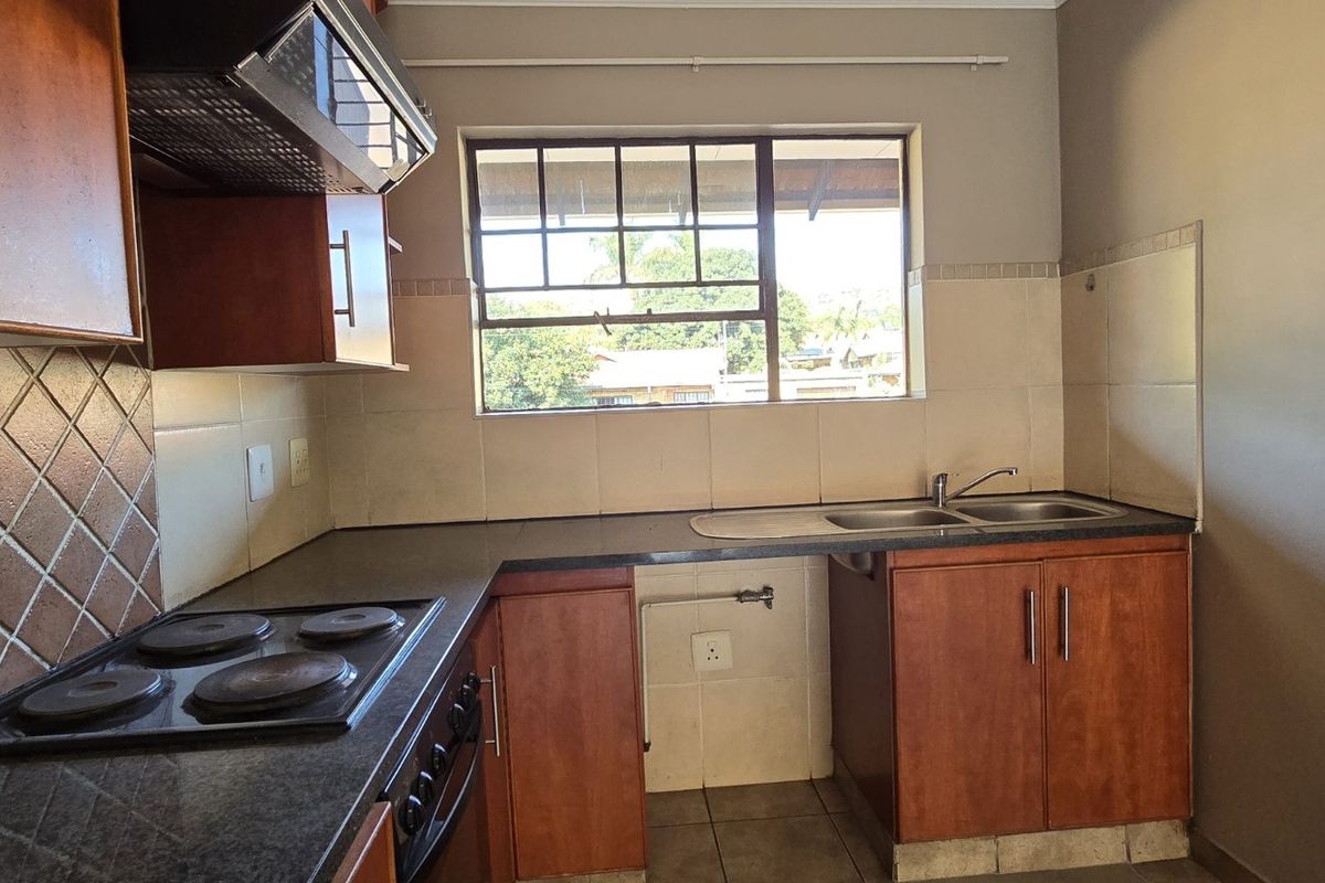 A functional kitchen featuring built-in wooden cabinetry, dark laminate countertops, an electric hob with extractor fan, and a double bowl sink.