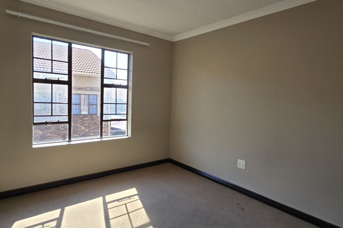 An empty bedroom featuring neutral wall paint, carpeted flooring, and a window with security bars, providing a blank canvas for personalization.