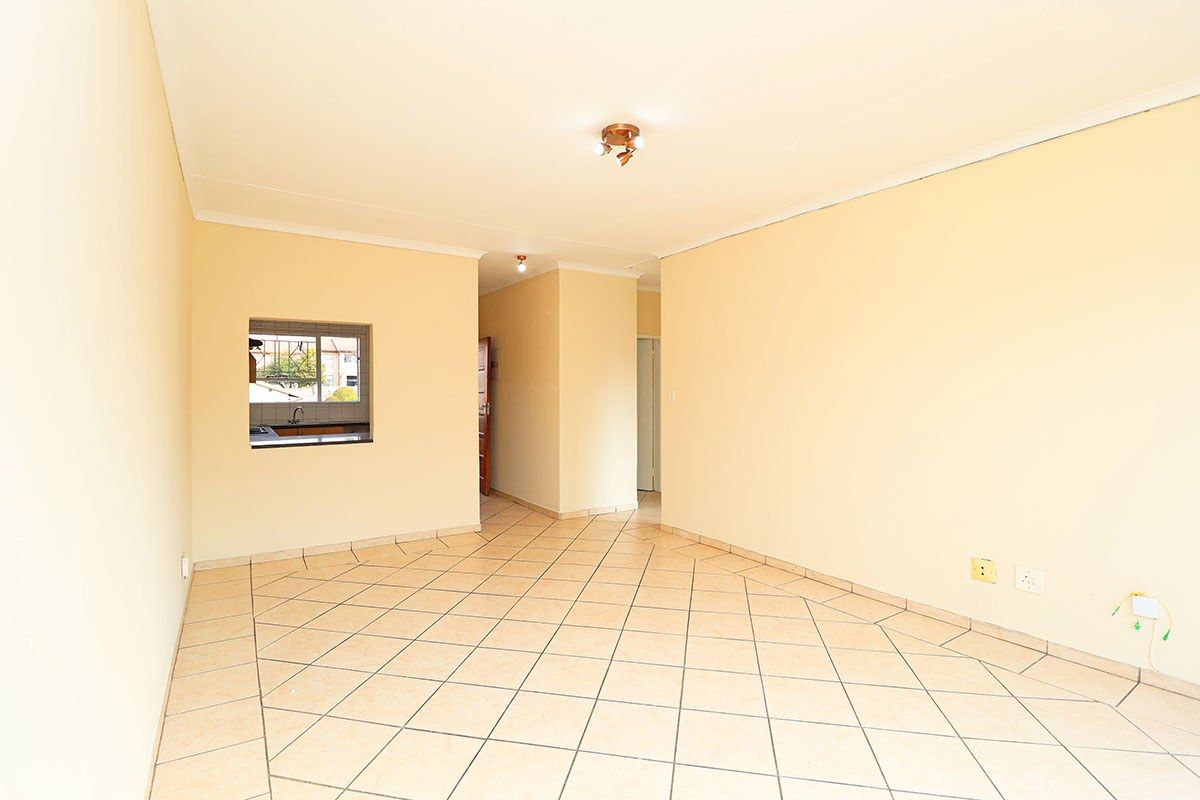 A spacious, empty living area featuring neutral walls, ceramic tiled flooring, and a convenient pass-through window connecting to the kitchen space.