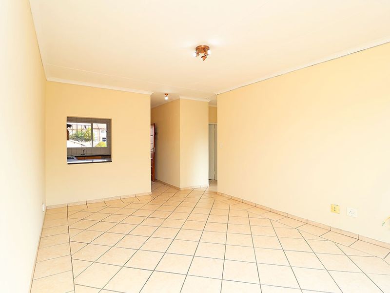 A spacious, empty living area featuring neutral walls, ceramic tiled flooring, and a convenient pass-through window connecting to the kitchen space.
