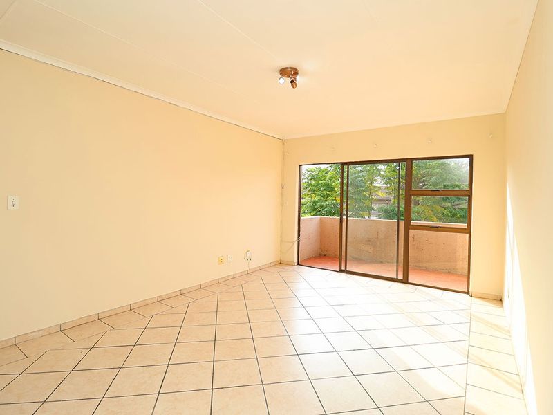 An empty, well-lit living room featuring tiled flooring and a sliding glass door providing access to an outdoor balcony area.