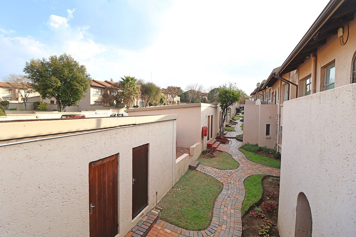 An elevated view of a townhouse complex featuring well-maintained brick pathways, landscaped garden beds, and stucco exterior walls.