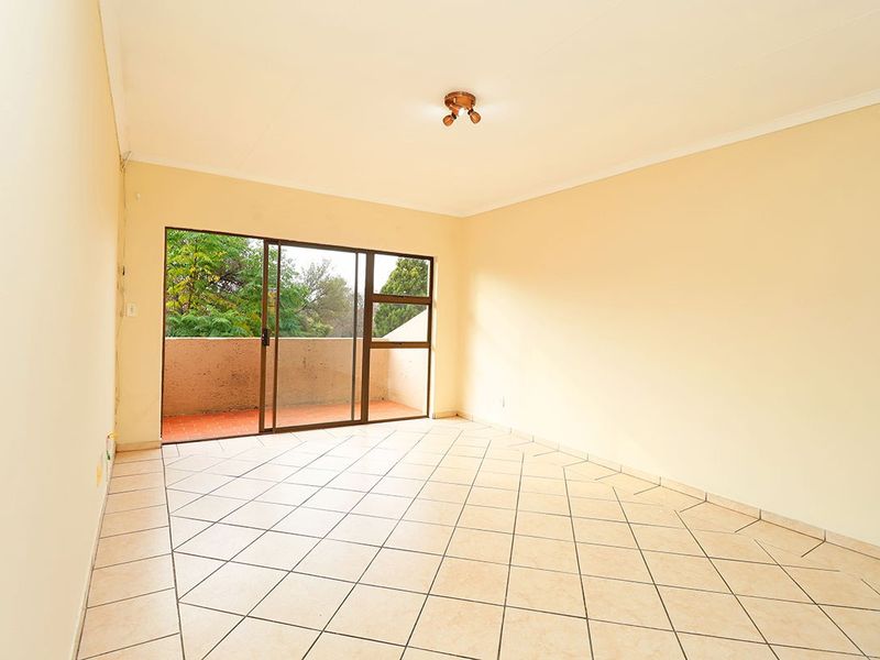 An empty, well-lit living room featuring neutral tiled flooring and a sliding glass door providing access to an outdoor balcony area.