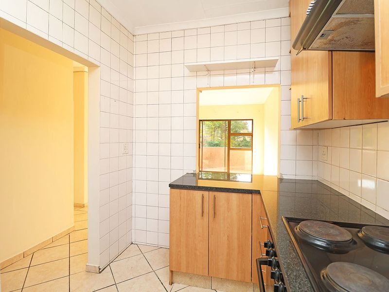 A functional kitchen featuring built-in wooden cabinetry, granite countertops, an electric hob with extractor fan, and tiled finishes throughout.