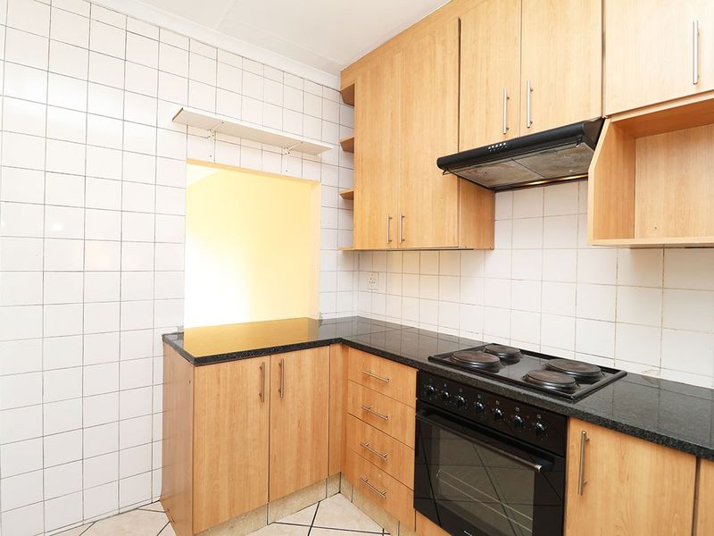 A functional kitchen featuring light wood-finish cabinetry, dark granite countertops, a built-in electric oven and hob, and white tiled splashbacks.