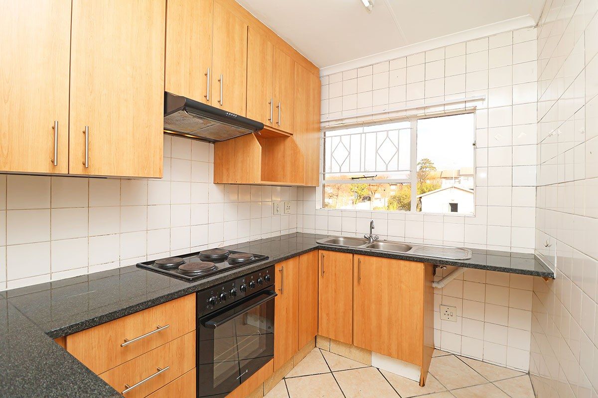 A functional kitchen featuring light wood cabinetry, granite countertops, a built-in oven with hob, and a double basin sink with tiled splashbacks.