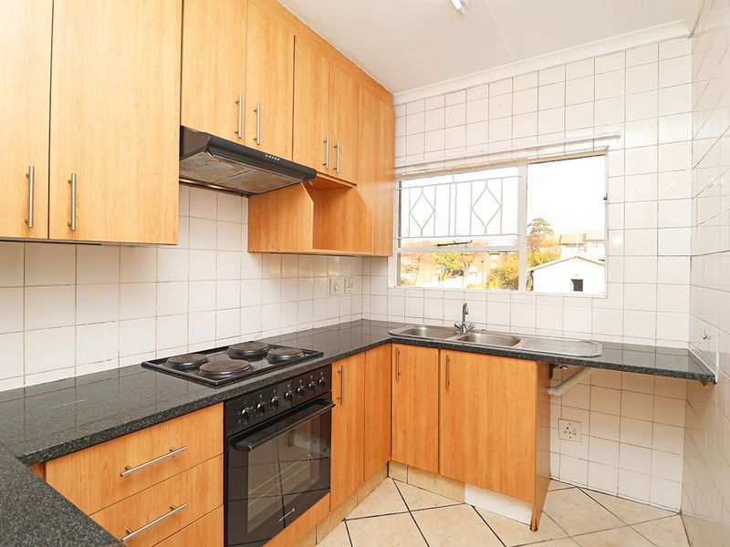 A functional kitchen featuring light wood cabinetry, granite countertops, a built-in oven with hob, and a double basin sink with tiled splashbacks.