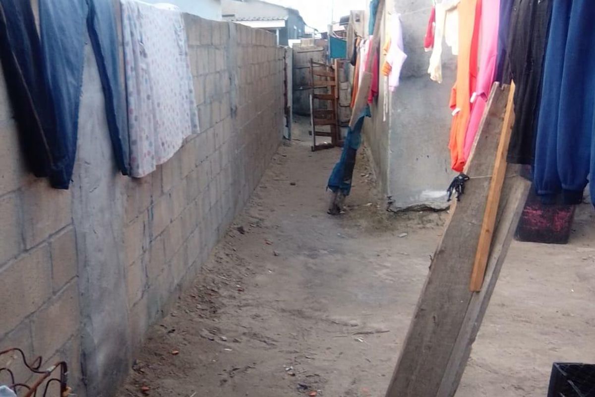 A narrow side passage between two structures featuring a concrete block boundary wall and unpaved ground.