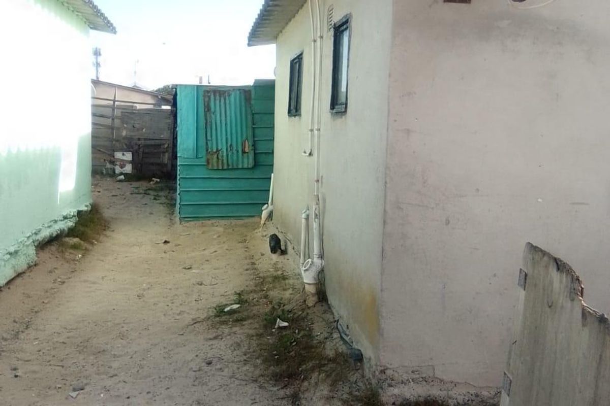 Side passage between two structures featuring corrugated roofing, external plumbing, and a satellite dish mounted on the exterior wall.