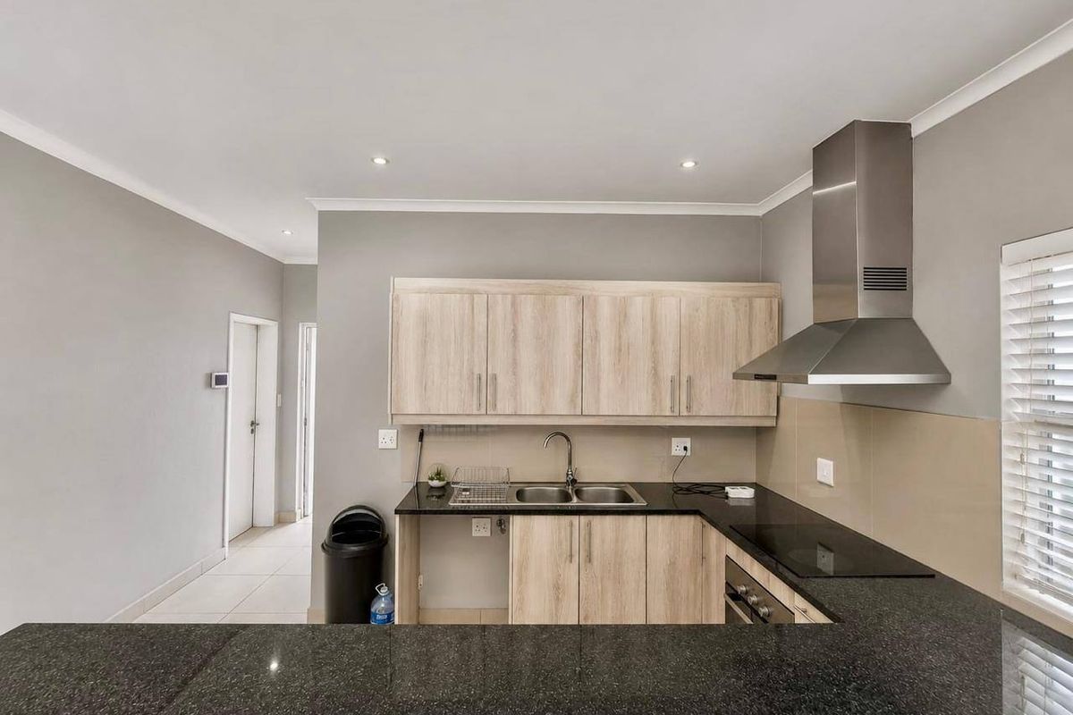 Modern kitchen featuring light wood-look cabinetry, dark granite countertops, integrated stainless steel appliances, and a breakfast bar overlooking the living area.
