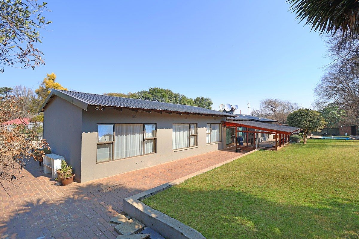 Rear view of the house featuring a metal roof, brick paved patio, and a covered veranda overlooking the garden area.