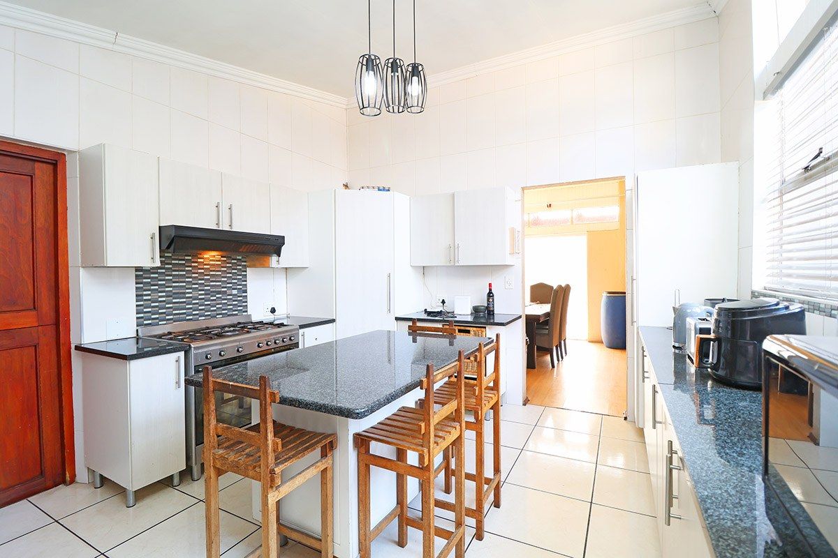 A functional kitchen featuring granite countertops, a gas stove with extractor fan, tiled finishes, and a central island with breakfast bar seating.