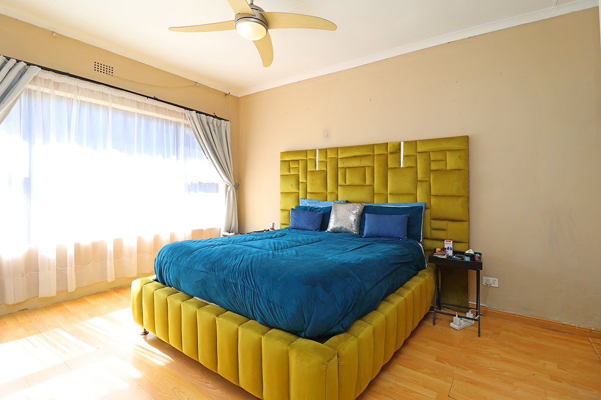 A spacious bedroom featuring laminate flooring, a ceiling fan, and large windows allowing for ample natural light.