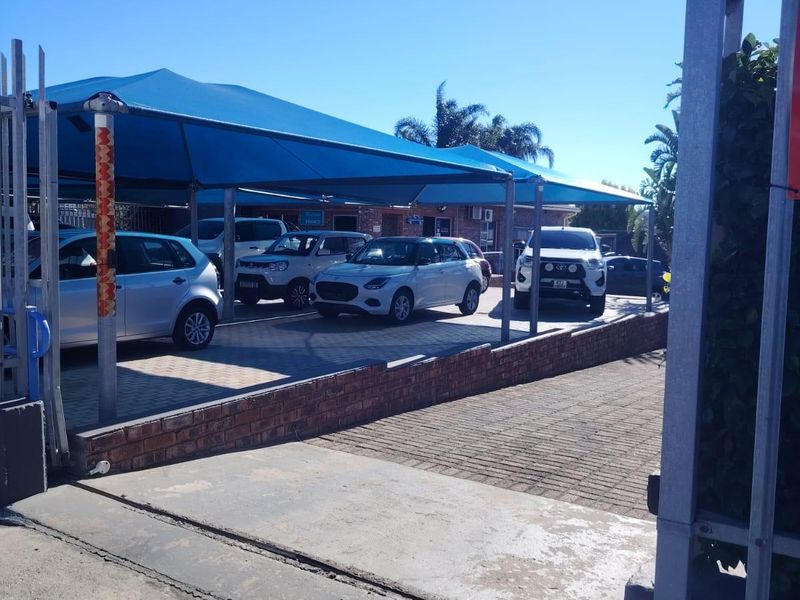 Commercial property frontage featuring a paved driveway, brick retaining wall, and a large blue shade cloth structure for vehicle parking.