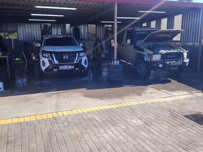 Commercial wash bay facility featuring a covered structure with integrated lighting, concrete flooring, and drainage systems, suitable for vehicle maintenance and cleaning operations.
