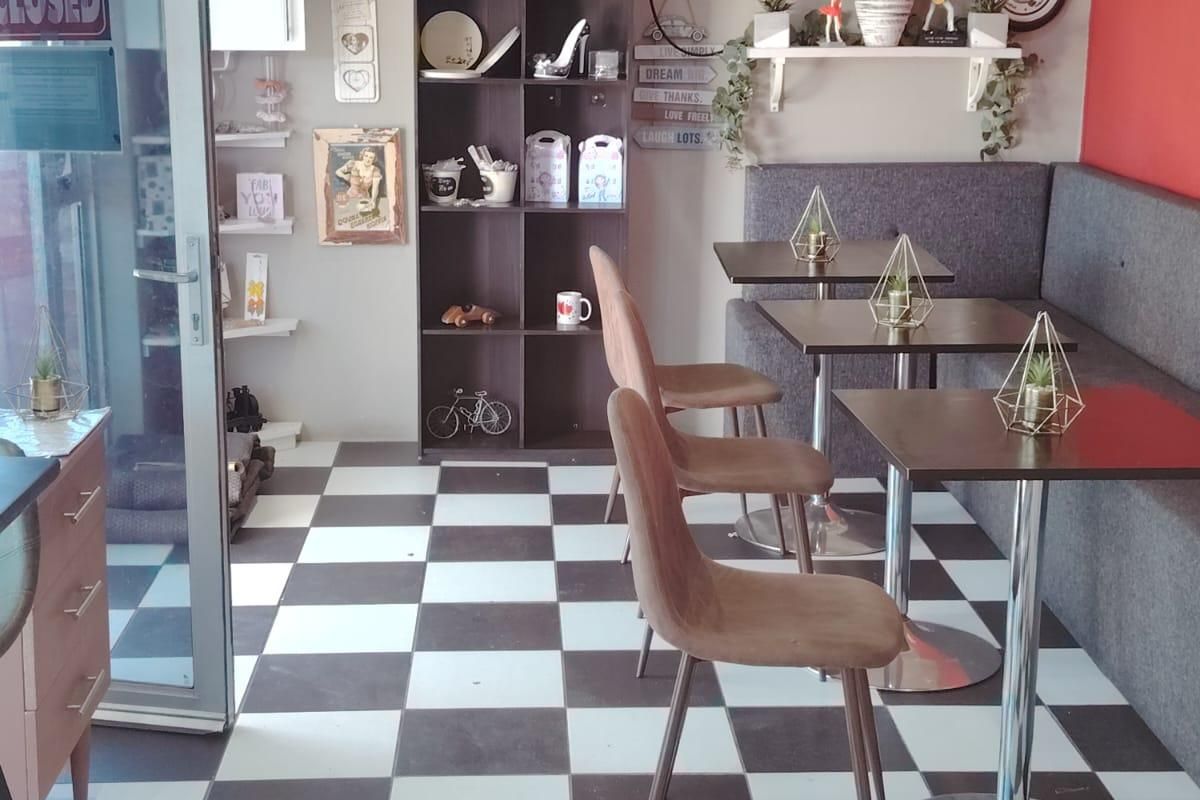 A commercial interior space featuring a checkered tile floor, built-in shelving, and a glass entrance door, currently set up with cafe-style seating.