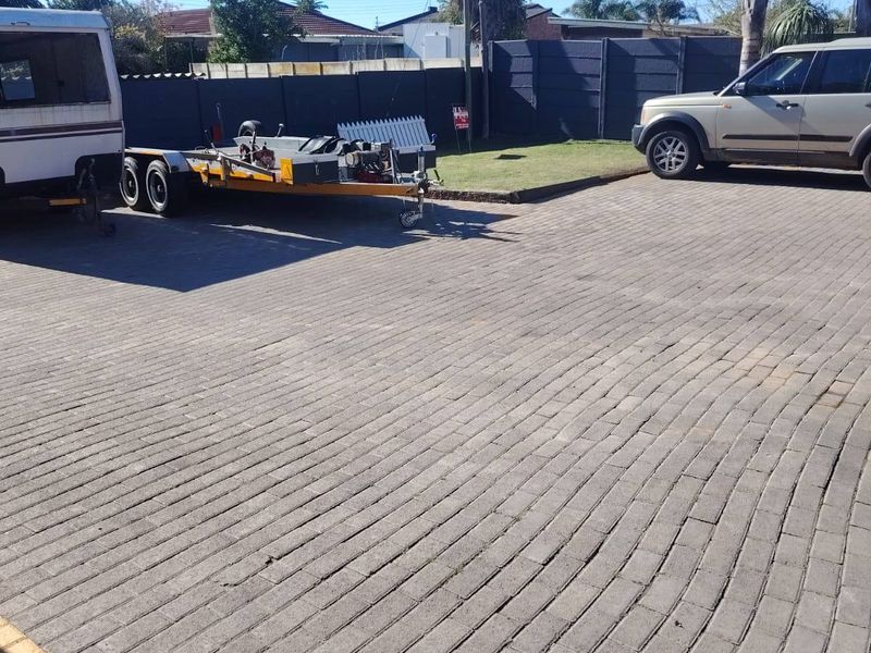 A paved driveway area providing ample parking space, enclosed by perimeter fencing and featuring established palm trees.