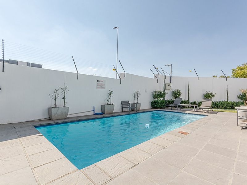 A well-maintained outdoor swimming pool area featuring a paved deck, perimeter wall with electric fencing, and exterior lighting.
