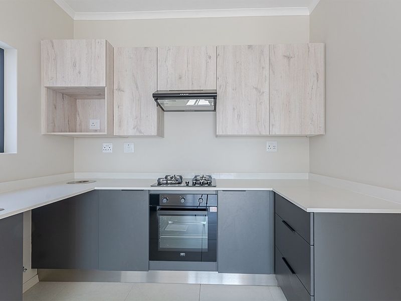 Modern kitchen featuring light wood-look upper cabinets, dark grey lower cabinetry, stone countertops, and integrated gas hob with oven.