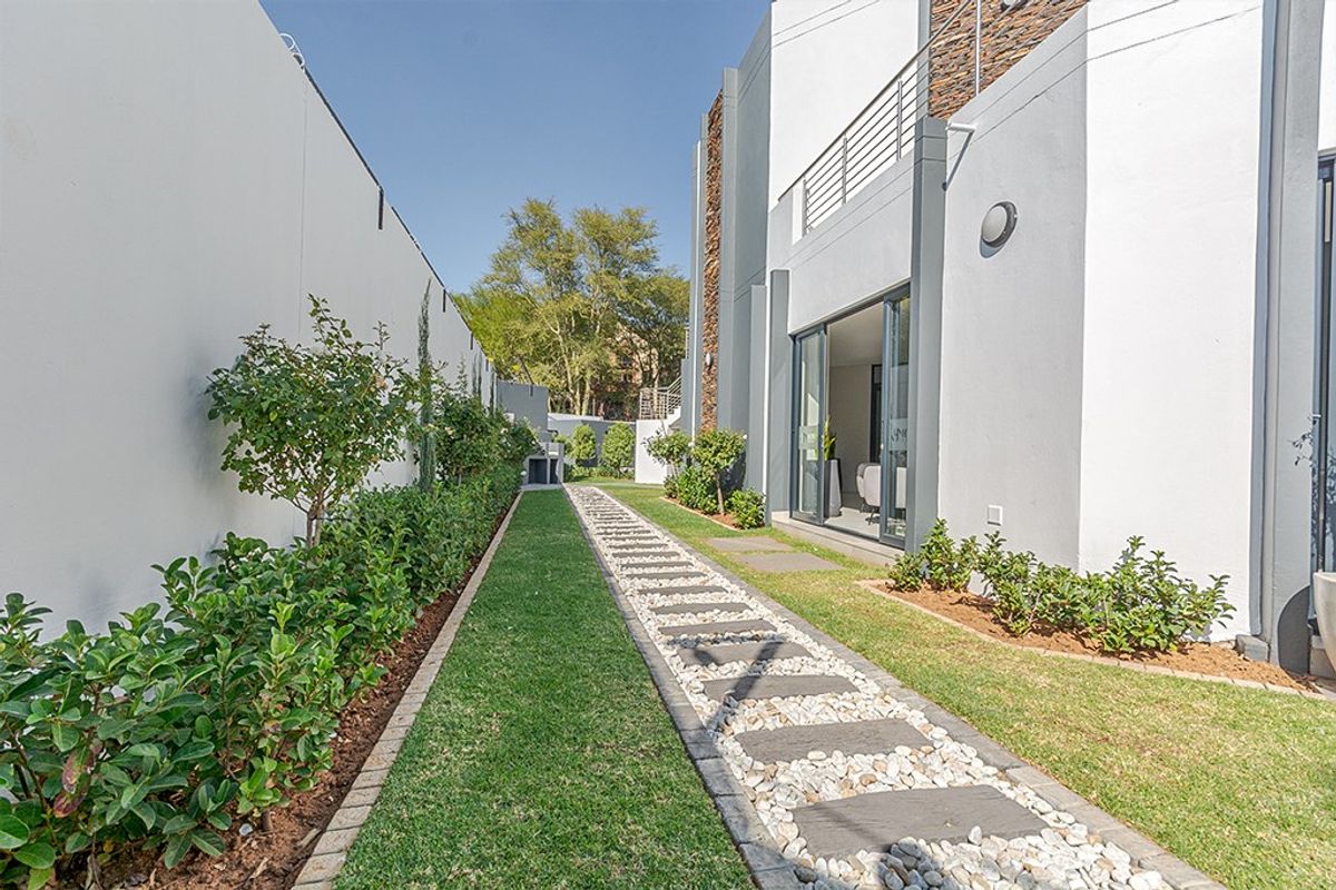 A well-maintained rear garden featuring a stone paver walkway, manicured lawn, and modern building facade with sliding glass doors.