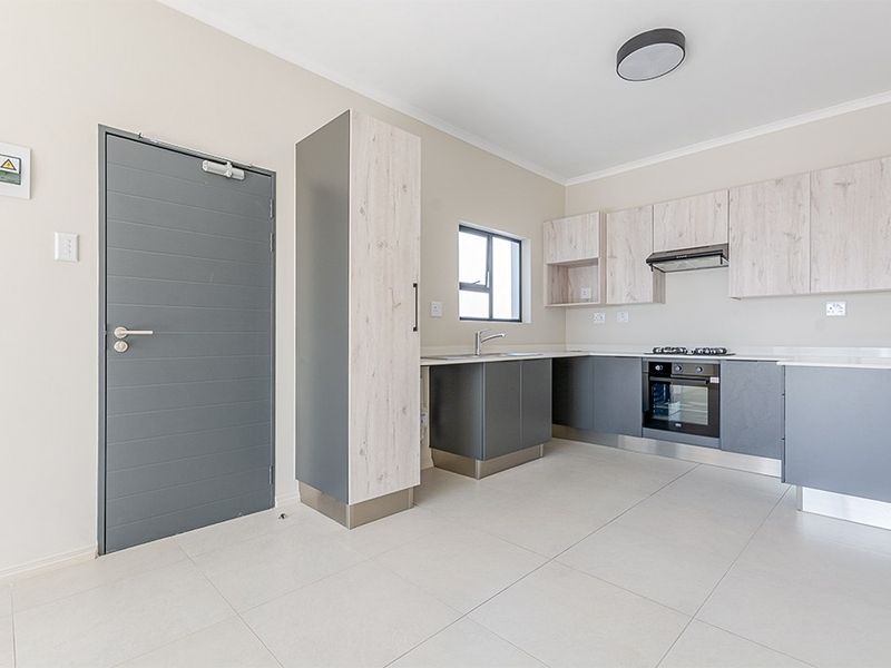 Modern kitchen featuring two-tone cabinetry, built-in oven and hob, extractor fan, and neutral tiled flooring in a clean, well-maintained space.