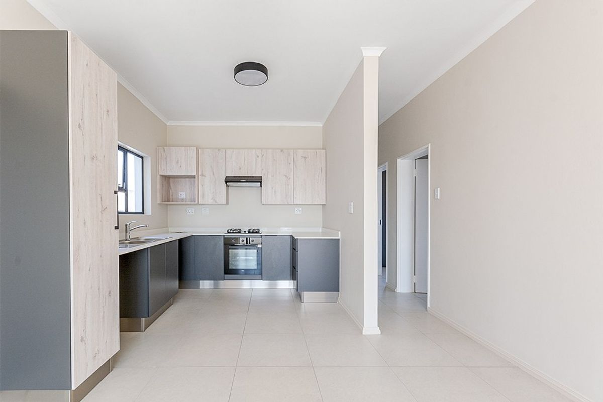 Modern kitchen featuring two-tone cabinetry, built-in oven, hob, extractor fan, and neutral tiled flooring in an open-plan layout.
