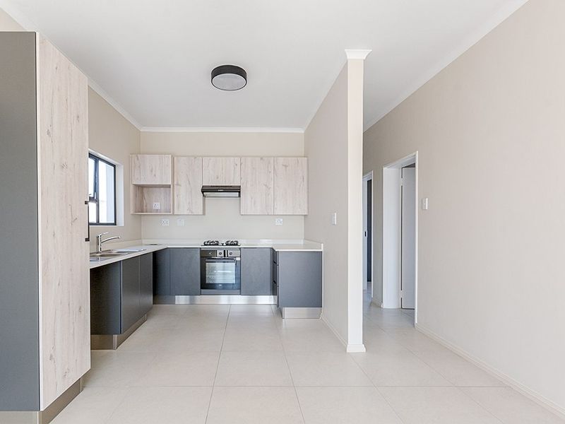Modern kitchen featuring two-tone cabinetry, built-in oven, hob, extractor fan, and neutral tiled flooring in an open-plan layout.
