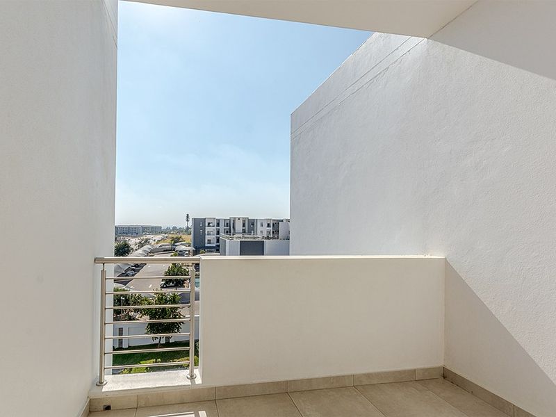 A clean, modern balcony featuring tiled flooring and a stainless steel balustrade, offering an open view of the surrounding apartment complex.