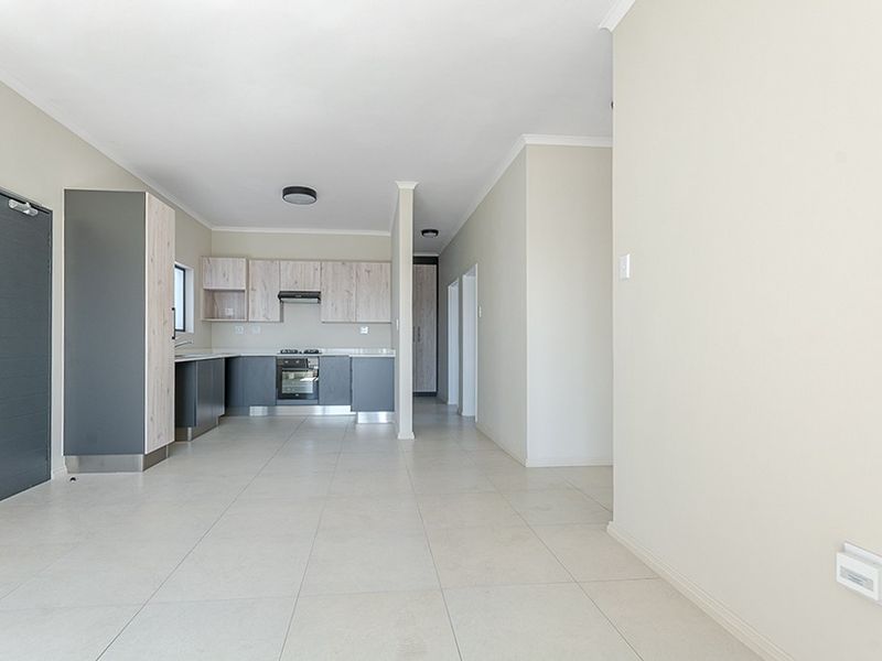 An open-plan living and kitchen area featuring modern two-tone cabinetry, built-in appliances, and neutral tiled flooring throughout.