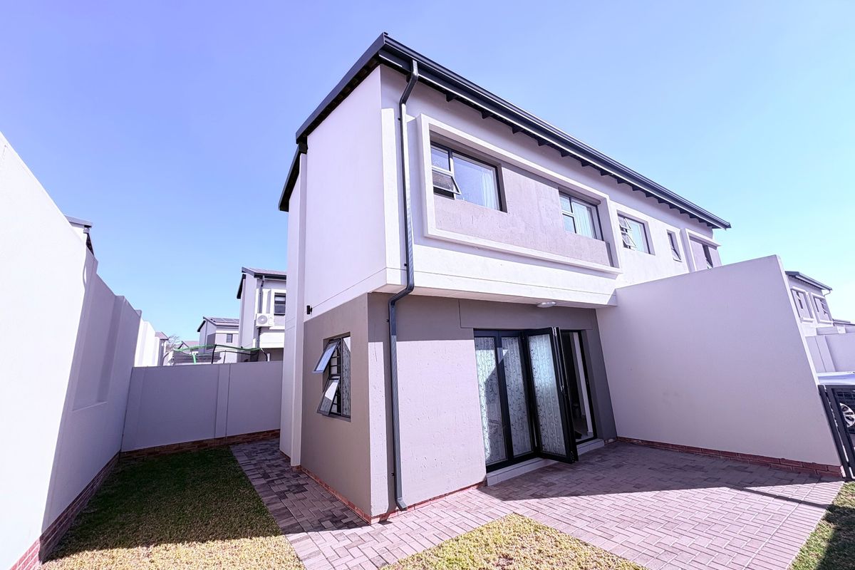 Rear view of a modern double-storey cluster home featuring a paved patio, private garden area, and secure boundary walls.