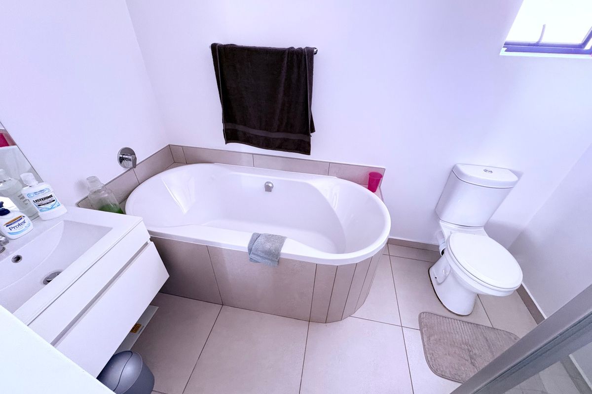 A clean, functional bathroom featuring a built-in bathtub, wall-mounted vanity with basin, and a standard toilet with neutral floor tiling.