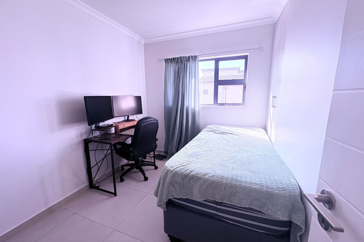 A functional bedroom featuring tiled flooring, built-in cupboards, and an aluminium window frame, suitable for use as a bedroom or home office.