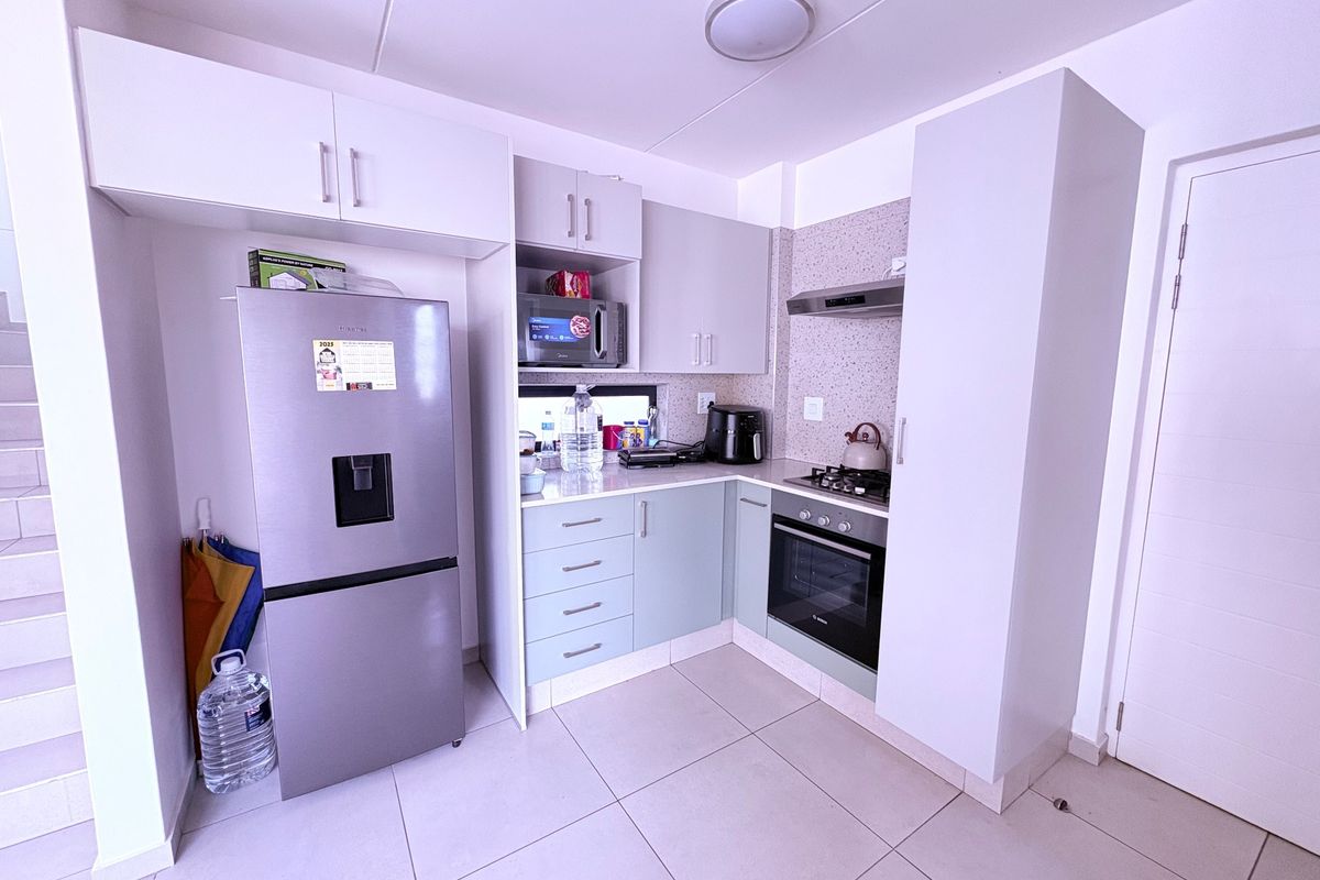 A modern, compact kitchen featuring built-in cabinetry, stone countertops, a gas hob, an electric oven, and an integrated extractor fan.