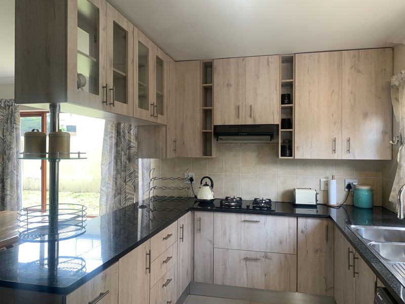 Modern kitchen featuring light wood-grain cabinetry, black granite countertops, a gas hob with extractor fan, and a functional double sink layout.