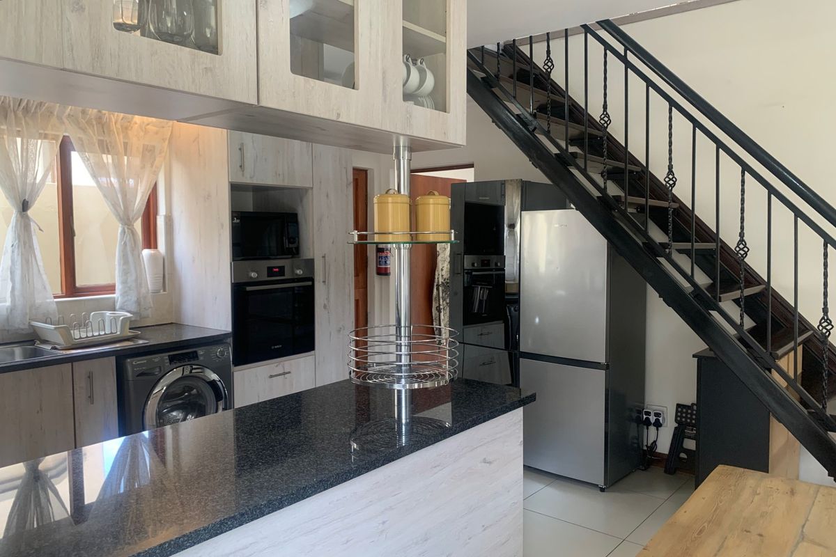 Modern kitchen featuring granite countertops, built-in appliances, and glass-front cabinetry, seamlessly integrated with an open-plan staircase design.