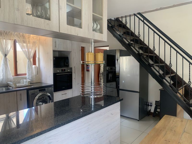 Modern kitchen featuring granite countertops, built-in appliances, and glass-front cabinetry, seamlessly integrated with an open-plan staircase design.