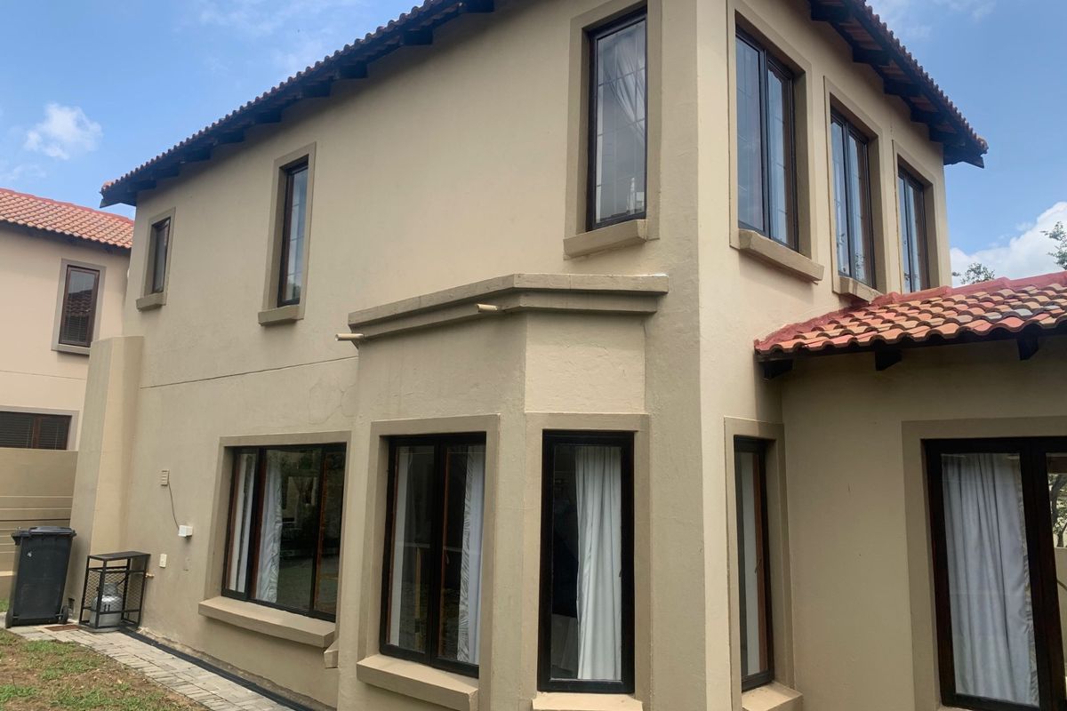 Rear exterior view of a double-story cluster home featuring terracotta roof tiles, plastered walls, and dark aluminium window frames.