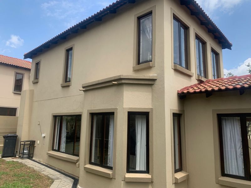 Rear exterior view of a double-story cluster home featuring terracotta roof tiles, plastered walls, and dark aluminium window frames.