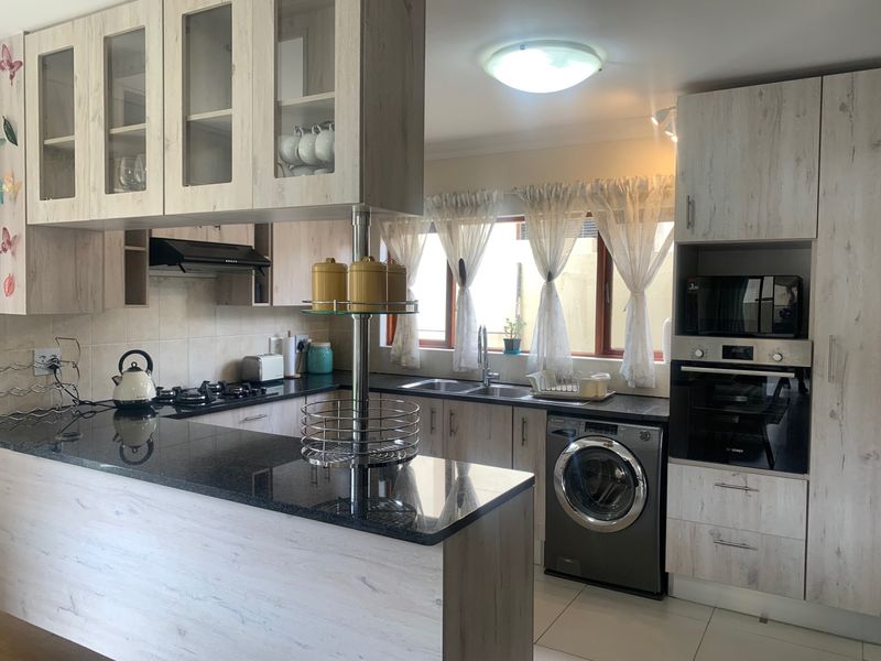 Modern kitchen featuring light wood-grain cabinetry, dark granite countertops, built-in oven, gas hob, and integrated laundry appliance space.