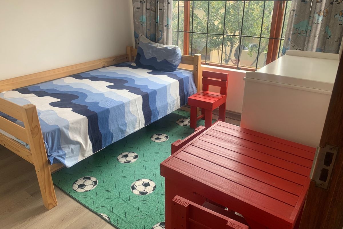 A functional bedroom featuring laminate flooring and large windows fitted with security burglar bars, providing natural light and a view of the exterior.