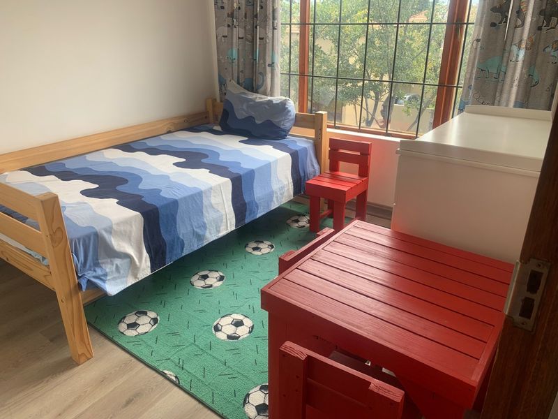 A functional bedroom featuring laminate flooring and large windows fitted with security burglar bars, providing natural light and a view of the exterior.