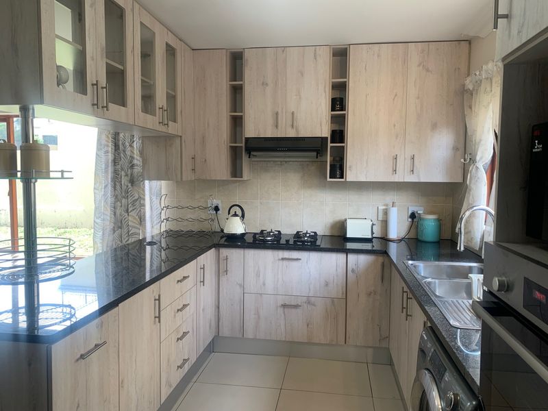 A well-maintained kitchen featuring light wood-grain cabinetry, dark granite countertops, a gas hob with extractor fan, and a double basin sink.