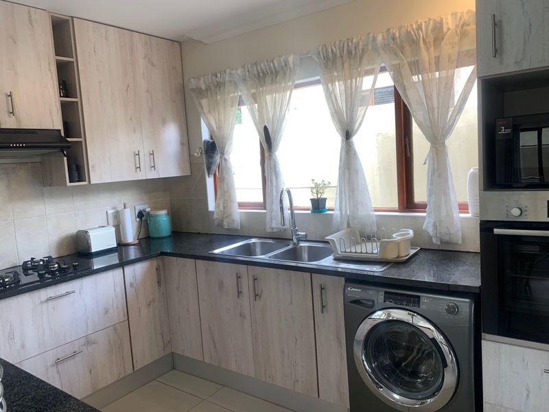A functional kitchen featuring light wood-grain cabinetry, dark granite countertops, a gas hob, built-in oven, and an integrated washing machine.
