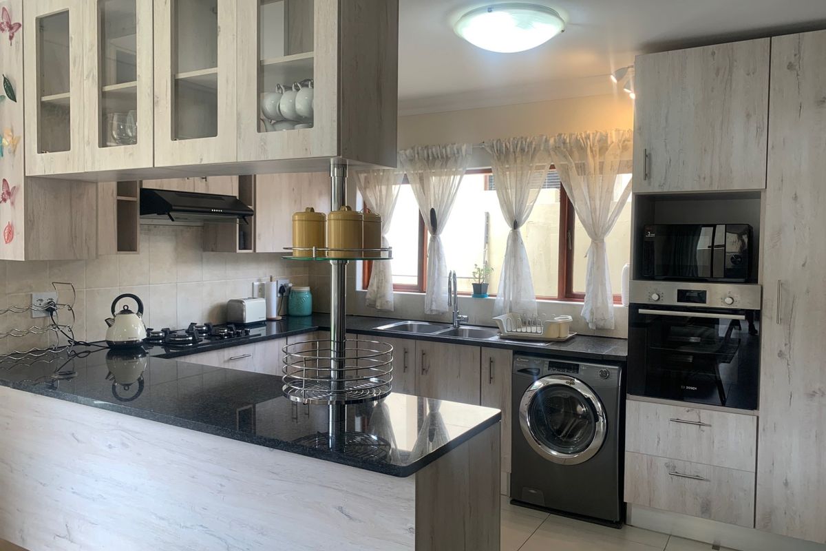 Modern kitchen featuring light wood-grain cabinetry, dark granite countertops, built-in oven, gas hob, and integrated laundry appliance space.