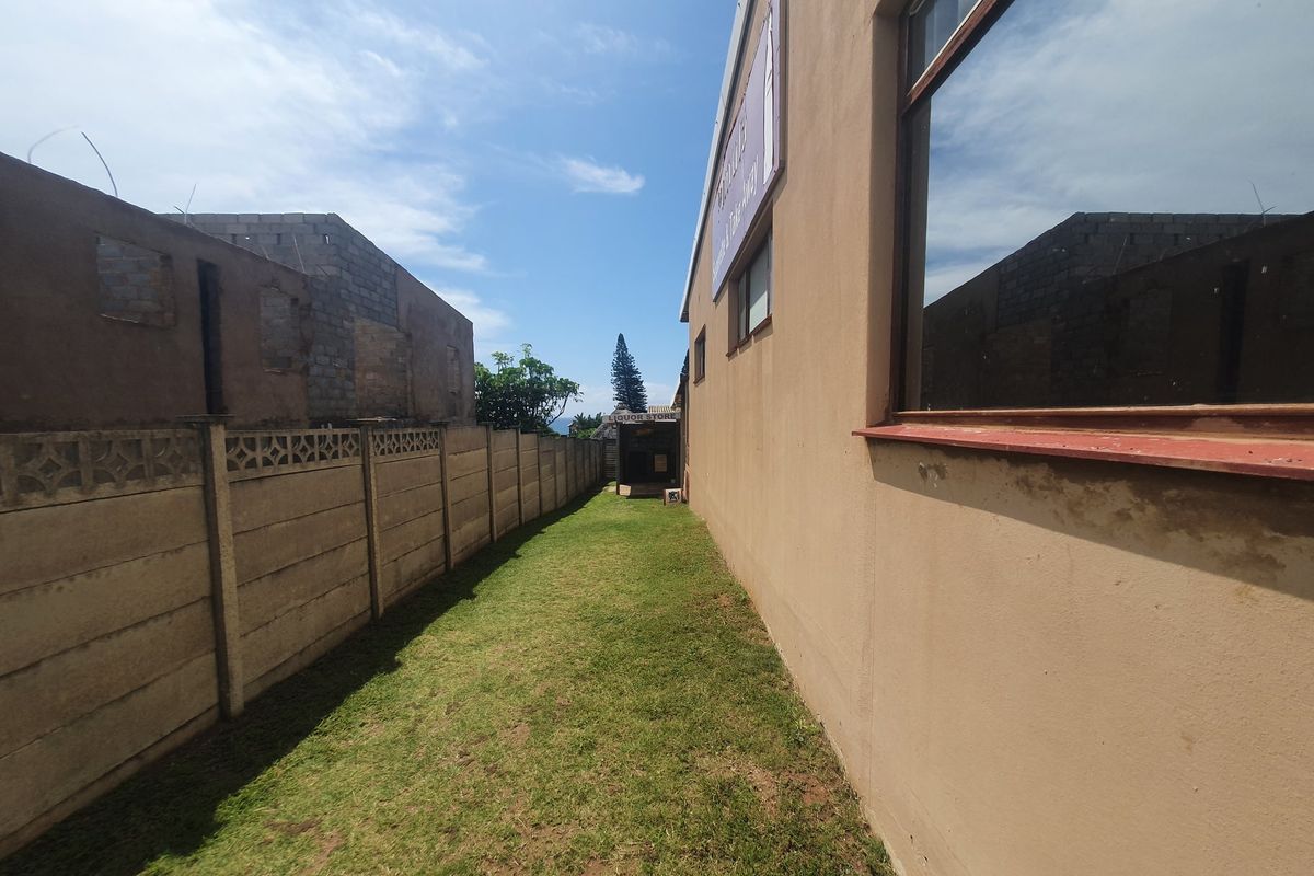 A narrow side passage of a commercial property featuring a precast concrete boundary wall, lawn area, and large windows along the building facade.