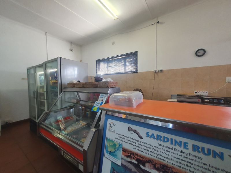 A commercial kitchen service area featuring a display fridge, stainless steel counter, and tiled splashback, suitable for food preparation or retail service.