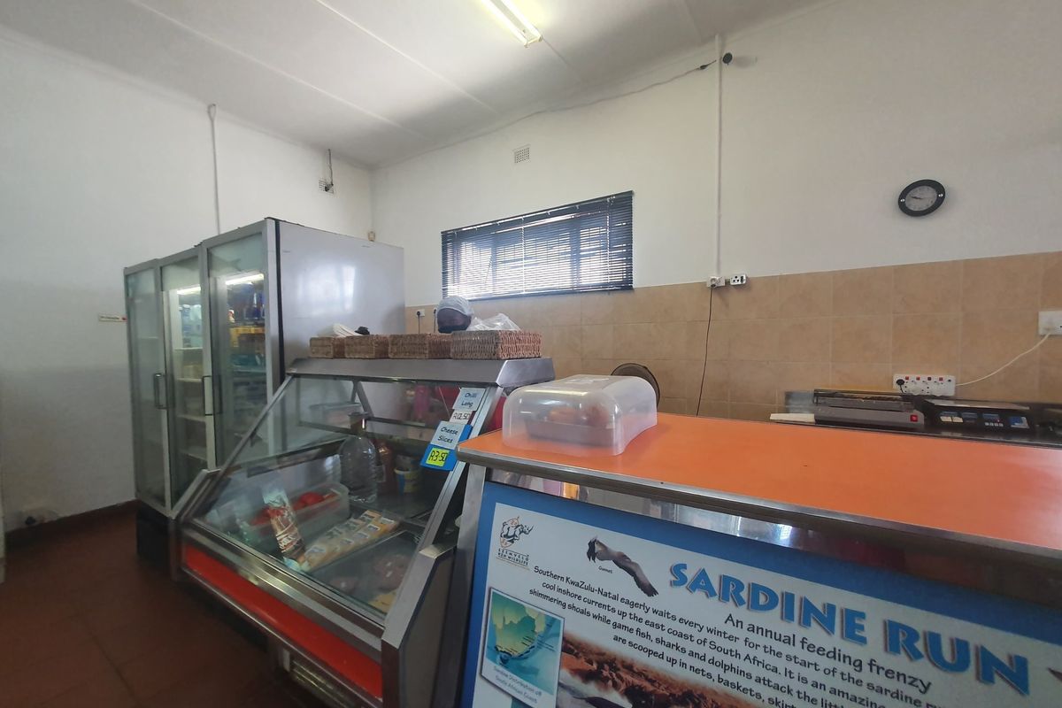 A commercial kitchen service area featuring a display fridge, stainless steel counter, and tiled splashback, suitable for food preparation or retail service.