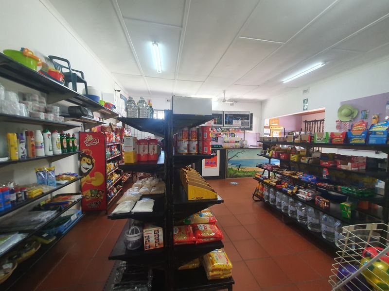 A commercial retail space featuring tiled flooring, fluorescent lighting, and a service counter, currently set up as a convenience store.