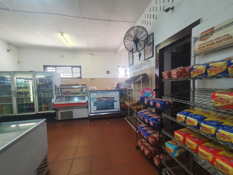 Interior view of a commercial retail space featuring tiled flooring, industrial wall-mounted fan, and functional retail display refrigeration units.