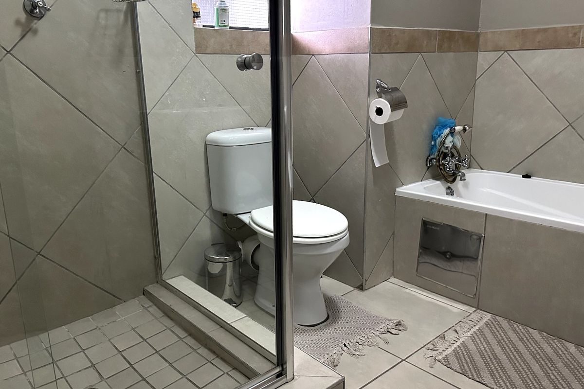 A functional bathroom featuring a glass-enclosed shower, a standard toilet, and a built-in bathtub with neutral wall and floor tiling.